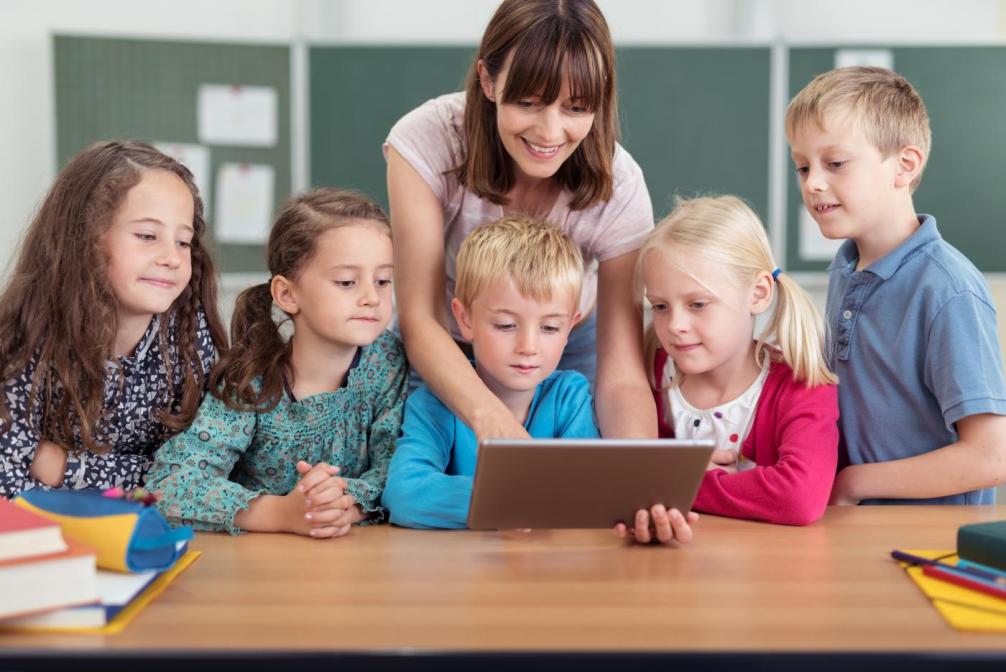 Symbolbild: Lehrerin zeigt vier Schülerinnen und Schülern etwas auf einem Tablet