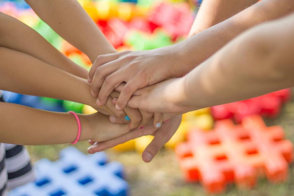 Symbolbild: mehrere Kinderhände, die sich berühren, dahinter mehrere Farben